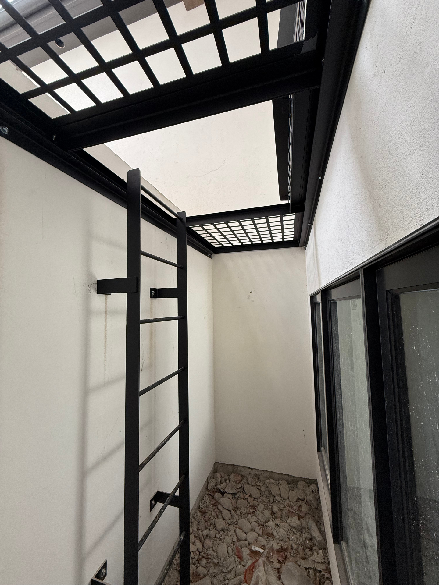 Blackened steel ladder and skylight grate in a light well