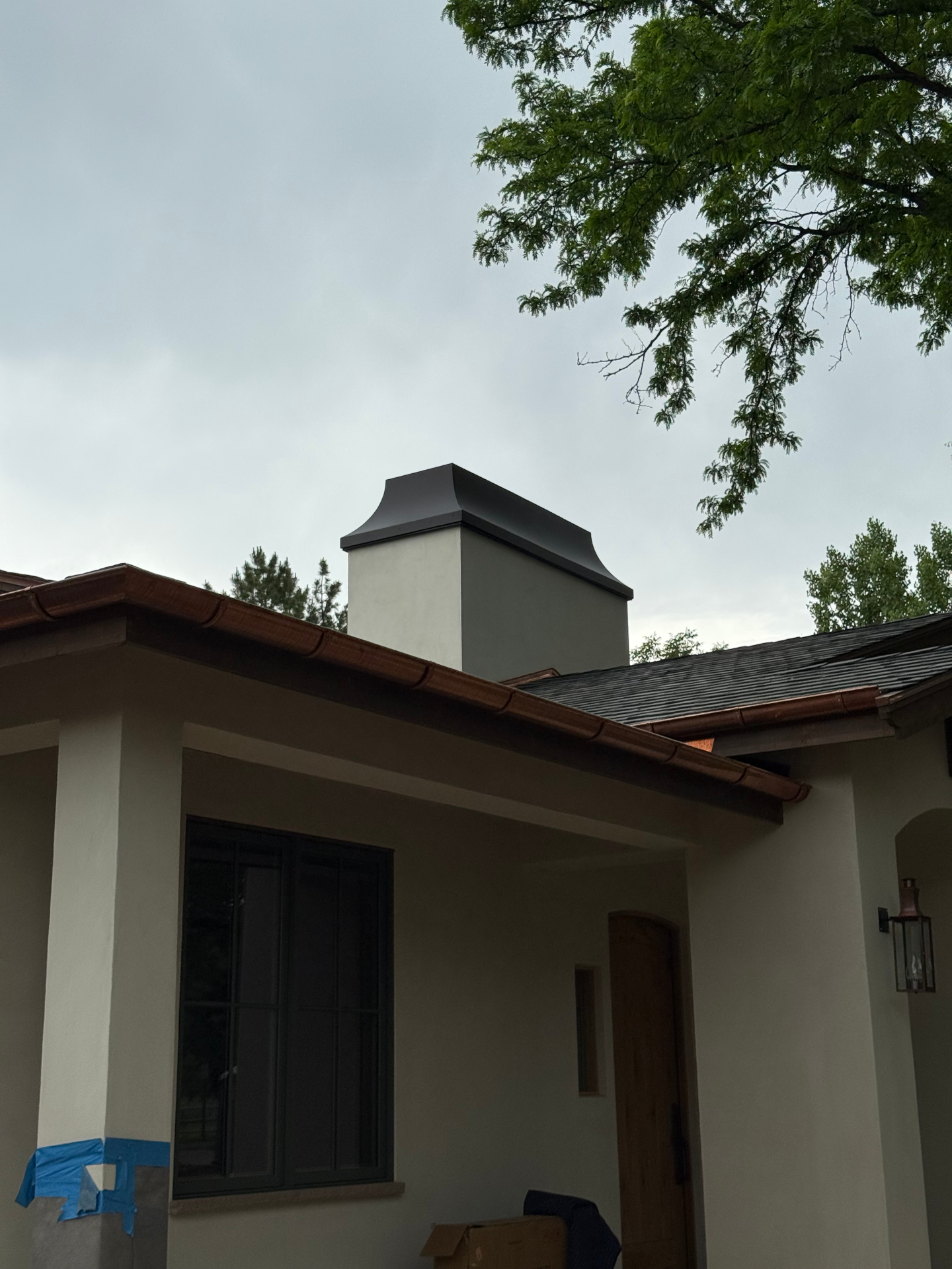 Custom blackened steel chimney cap on a stucco home